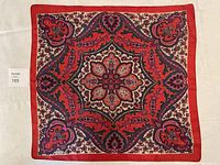 Full view of scarf showing overall paisley and floral design in red, black, pink and cream with solid red border.