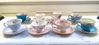 Eight vintage teacups and matching saucers in variety of colors and floral patterns arranged side by side