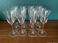 Front view of 12 clear wine glasses arranged in rows, showing classic flared rim and slender stems. One glass with a chip is visible.