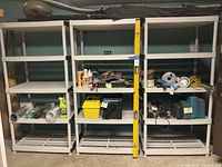 Three gray plastic shelving units side by side with some assorted items on shelves.