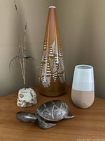 Photo showing four items: metal wire art sculpture with rock base, tall brown and white hand-blown glass vase, pottery vase with cream glazed top, and wood turtle carving.