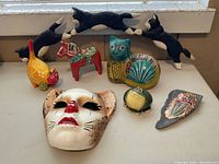 Overview of all figurines and decorative items including painted ceramic cat mask, wood cat arches, hand-painted horse figurine, terra cotta cat, frog, chicken and flower piece.