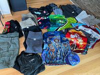 Overview photo of the lot showing folded pants, shorts, cycling jerseys, and long sleeve shirts arranged on wooden floor