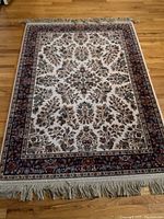 Full view of Karastan wool area rug with ivory Sarouk pattern and fringe tassels, placed on wood floor.