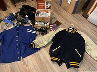 Men's letterman jacket, wool sweater, shoe kit and grooming tools spread on floor