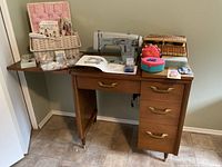 Front view of mid-century wood sewing cabinet with White sewing machine, baskets, and notions on top, showing cabinet extended with one side open
