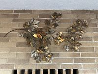 Full view of large metal branch sculpture with multiple maple leaves mounted on brick wall.