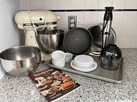 Photo showing entire lot including KitchenAid Hobart stand mixer, Cuisinart Smart Stick hand blender, metal mixing bowl, baking pans, ramekins, and kitchen scale all arranged on kitchen counter.