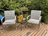 Wide shot showing two chairs, side table, plant stand, watering can, birdhouse, turtle figurine