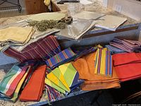 Photo showing multiple folded napkins in various colors including orange, striped multi-color, yellow, and blue, along with multi-color striped and orange fabric pieces.