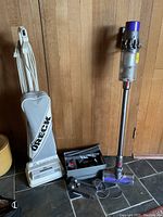 Oreck XL upright vacuum and Dyson Cyclone V10 stick vacuum side by side with accessories and power cord showing.