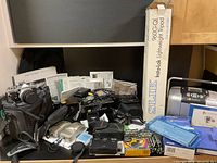 Overview of all lot contents: cameras, manuals, tripod box, printer, film packs and accessories on countertop