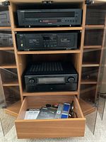 Full shot of Yamaha and Denon stereo components stacked in wooden shelving with manuals, remotes, and wires in drawer.