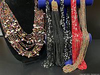 Full set of six colorful artisan bohemian glass bead necklaces alongside one black beaded necklace with an antique coin clasp shown on display stand and necklace holder