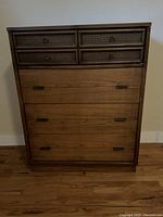Front view of vintage wood chest of drawers showing rattan accent on top drawers and laminate top surface.
