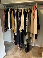 Closet rack showing various women's clothing items in different colors and styles hung on hangers including jackets, skirts, dresses, and tops.