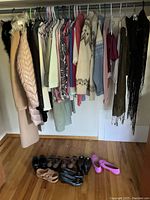 Closet rod with variety of women's clothing hung on hangers and pairs of shoes aligned on the floor