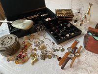 Display of many jewelry items, three vintage boxes, perfume bottles, and accessories arranged on a white lace tablecloth