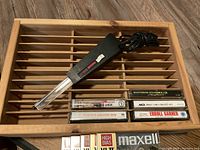 Wooden cassette tape holder with a cassette tape cleaner and several vintage cassette tapes displayed on it.