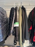 Side view of 7 blazers hanging on a rack, some partially covered with plastic garment bags, showing variety of textures and patterns.