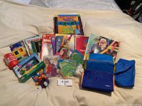 Photo of entire lot showing Barrel of Monkeys toy, children’s books, colored pencils, yarn doll, and craft fabric pieces.