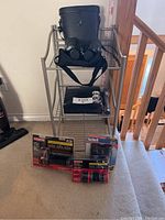 Full view of the rack holding a pair of large black binoculars in a case on top shelf, three boxed flashlights on lower carpeted floor in front