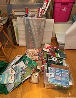 Wide view of boxed and bagged Christmas gift bags, gift tags, and rolls of wrapping paper arranged on floor