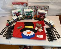 Overview of train set, tracks, boxes of ornaments, santa sled with reindeer, and tree skirt, arranged on table.