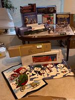 Full lot overview showing boxed Christmas Village Scene with rotating train, boxed light-up garlands, decorative holiday mats, and assorted Christmas decor
