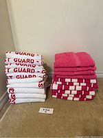 Rolled white towels with red 'Coast Guard' text stacked on left; folded pink and pink & white checkered towels on right.