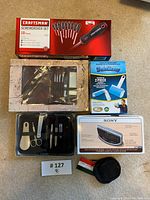 Top view showing all items including the Craftsman screwdriver set box, grooming kit in black plastic case, Sony alarm clock box, lint rollers and pouch.