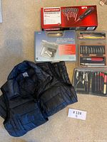 Overview of the lot showing the Craftsman screwdriver set, staple gun in box, small crafting tools, blades, and black vest laid out on floor.