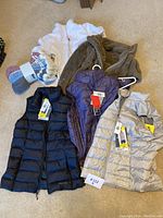 Lot of 3 Eddie Bauer puffer vests, 2 fleece jackets, and BENCH socks arranged on carpet
