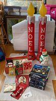 Pair of red Noel blow mold lights alongside boxed Christmas decorations and light boxes on floor.