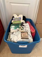 Top view of blue plastic bin containing the throws and housecoat, showing all items packed together.