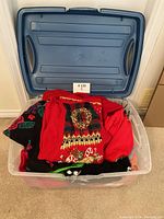 Blue storage bin containing folded sweaters and cardigans, predominantly red Christmas-themed knitwear visible.