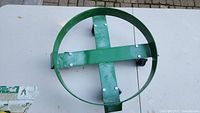 Top view of green steel circular dolly frame with central crossbar and bolt attachments.