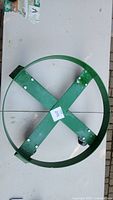 Top view of green metal dolly showing circular outer ring and X-shaped crossbars with label