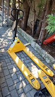 Full view of yellow AltraLift pallet jack showing the handle, frame, and fork tines on a paved outdoor surface.
