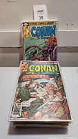 Stack of Conan The Barbarian comic books with visible colorful covers, a Marvel Comics Group logo on the top, and different illustrations of Conan in action scenes.