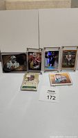 Wide shot showing six football trading cards in protective holders arranged on a white surface. Cards include Dan Marino, Tom Brady, Ben Roethlisberger, Drew Brees, and Shawn Bledsoe.