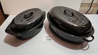 Photo showing two black speckled roasting pans with lids on white surface, one smaller and one larger
