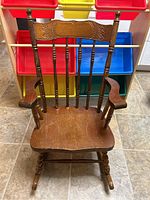 Front view of antique child's wooden rocking chair showing carved back rest and armrests