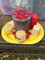 Mixed lot of candles arranged on a yellow tray including large purple pillar candle with red tealights on top, two round yellow banded candles, tall red rectangular candle, and small white square candle.