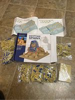 Photo of puzzle pieces sorted, folded instruction manuals showing detailed assembly steps, and box with image of completed Egyptian Sphinx model