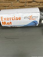 Photo showing the Maximo Fitness branded packaging of the exercise mat with label 'Exercise Mat' visible, wrapped in plastic.