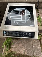 Front view of the Iwatani induction cooker showing the stainless steel and black glass top surface with brand marking and induction coil design.