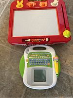 Photo of two kids educational toys: red Etch A Sketch and French talking learning tablet with screen and buttons.