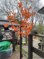 Full view of the approximately 5ft 4in tall LED maple tree with vibrant orange and red leaves outside on a deck area.