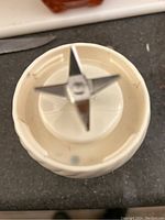 Close-up of white base unit showing four-pronged stainless steel blade attachment for blending.